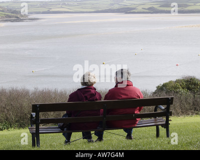 Vecchia coppia seduto su una panchina nel parco acquista il Memoriale di guerra a Padstow, affacciato sul fiume Camel, Padstow, Cornwall, Regno Unito Foto Stock