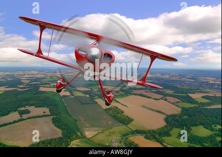 Un rosso biplano acrobatico in volo sopra il paesaggio rurale Foto Stock