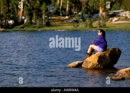 Donna seduta su roccia sulla riva del lago Boothe gamma Cattedrale Sierra Nevada Parco Nazionale Yosemite in California Foto Stock