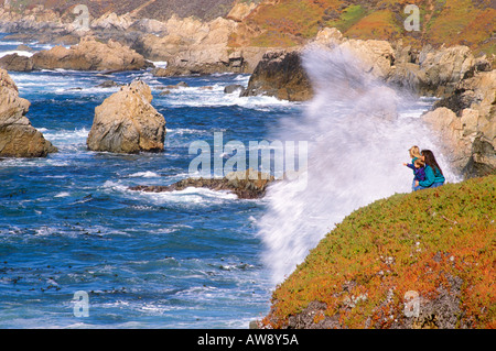 Madre e bambini (di età compresa tra 5 e 2) guardando surf pesante da un promontorio sulla costa del Pacifico Big Sur in California Foto Stock