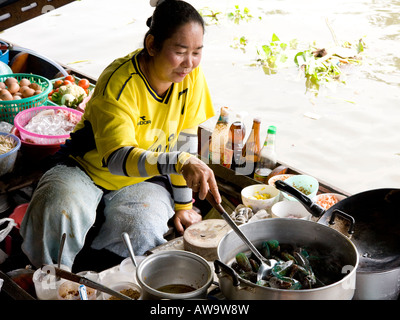 Donna Thai per la cottura rosolare in un wok a Bangkok mercato galleggiante della Thailandia del sud-est asiatico Foto Stock