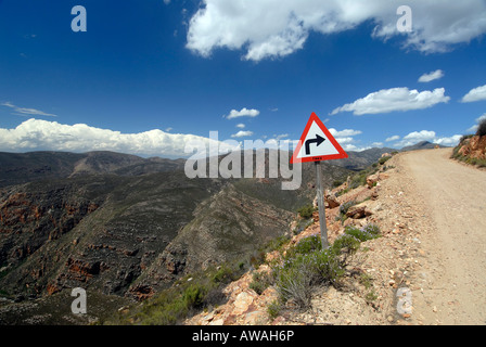 Un segno che indica una curva ad angolo retto su un suolo pietroso mountain pass road Foto Stock