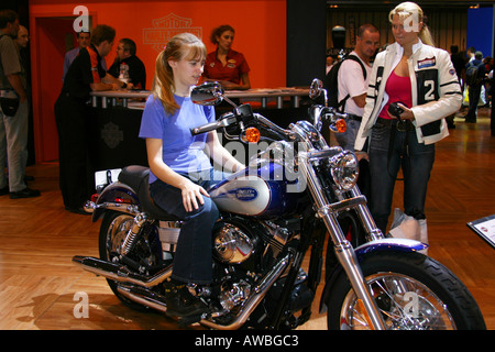 Ragazza seduta sulla Harley Davidson Moto mentre amico orologi al Motor Cycle Show al NEC di Birmingham. Foto Stock