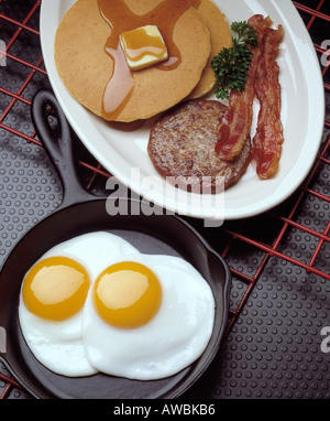 La colazione assortimento due uova fritte suny su lato rfi padella pila di frittelle salsicce patty due strisce di bacon burro fuso Foto Stock