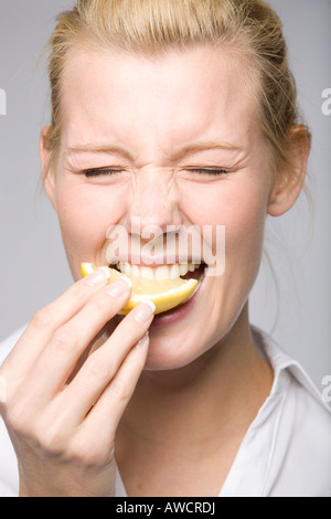 Giovane donna di mordere in un limone e facendo una faccia buffa Foto Stock