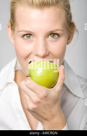Giovane donna bionda di mordere in una mela verde Foto Stock