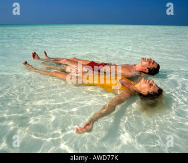 Coppia giovane rilassante in acque poco profonde, spiaggia, Maldive, Oceano Indiano Foto Stock