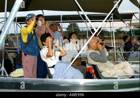 Turisti asiatici con il binocolo su un game drive in una barca sul fiume Chobe, Chobe National Park, Botswana Foto Stock