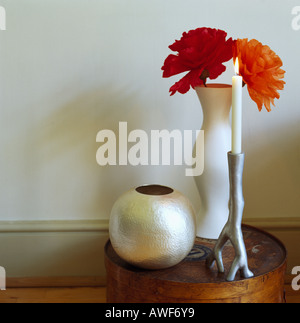 Close-up di garofani rossi in alto vaso bianco accanto al vaso di forma sferica e metallo candelabro con candela accesa Foto Stock