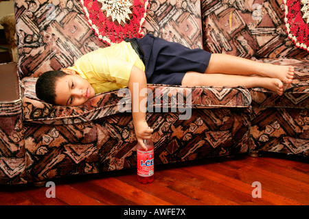 Ragazzo che indossa uniformi scolastiche posa su un divano, annoiato, Georgetown, Guyana, Sud America Foto Stock