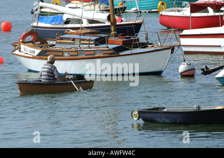 L'uomo canottaggio una piccola barca tra imbarcazioni da diporto ormeggiata in porto Groomsport, County Down, Irlanda del Nord Foto Stock