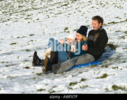 divertimento per tutta la famiglia su slitta, slitta, discesa sulla neve, padre, madre, bambino di un anno, ridere Foto Stock