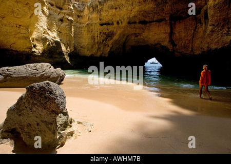 Una donna cammina su una spiaggia all'interno di una grotta lungo il Portogallo Algarve costa. Foto Stock