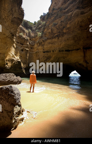 Una donna cammina su una spiaggia all'interno di una grotta lungo il Portogallo Algarve costa. Foto Stock