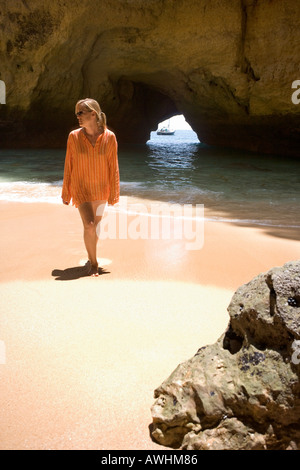 Una donna cammina su una spiaggia all'interno di una grotta lungo il Portogallo Algarve costa. Foto Stock