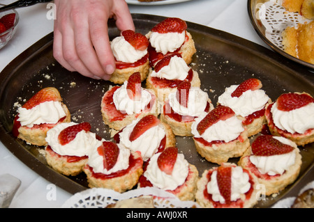 Donna di mano protesa per cornetto con marmellata e panna montata e fragole fresche al ricevimento di nozze a buffet con tè Foto Stock