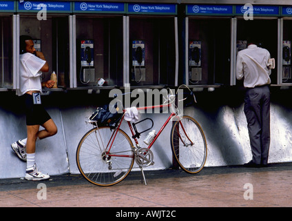 NY, NY, due uomini utilizzano telefoni a pagamento, uno con la bici Foto Stock