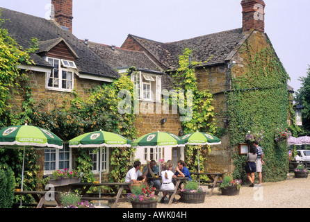 Lyddington Leicestershire Rutland persone mangiare bere al di fuori del paese di lingua inglese pub Inghilterra UK tabelle menu ombrelloni di lettura Foto Stock