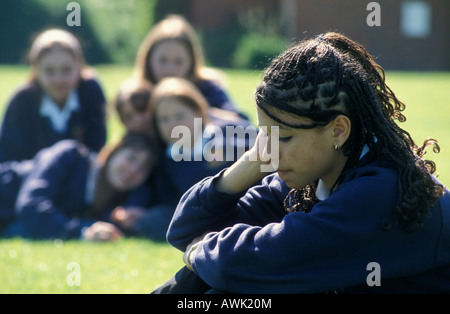 ragazza della scuola superiore in uniforme di origine mista tormentata da un gruppo di coetanei nel campo di gioco scolastico Foto Stock