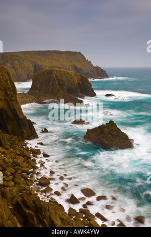 Scogliere vicino al Lands End Cornwall con il Enys Dodnan rock formazione in background Foto Stock