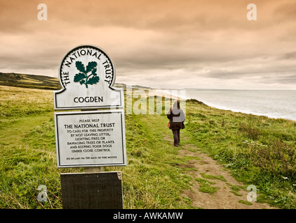 Donna passeggiate lungo le scogliere a Cogden spiaggia a Burton Bradstock, Dorset, England, Regno Unito con il segno NT Foto Stock
