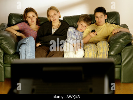 Focus sui giovani adulti e bambini seduti sul lettino in background, vista posteriore della televisione in primo piano sfocato. Foto Stock