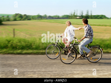 L uomo e la donna in bicicletta, tenendo le mani, campagna in background Foto Stock