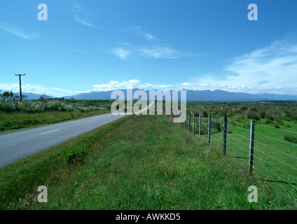 Nuova Zelanda, strada attraversando grassy area rurale, la gamma della montagna di distanza Foto Stock