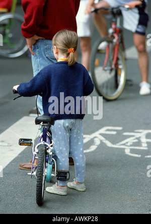 Bambina in piedi accanto a bicicletta in bikelane, vista posteriore Foto Stock