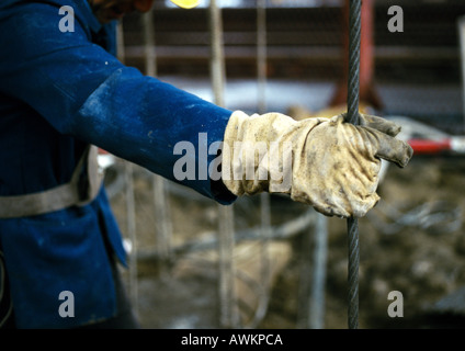 Persona con mano guantata cavo di contenimento sul sito in costruzione, close-up Foto Stock