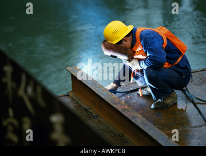 Saldatore di indossare la maschera di saldatura, accovacciato e trave di saldatura Foto Stock