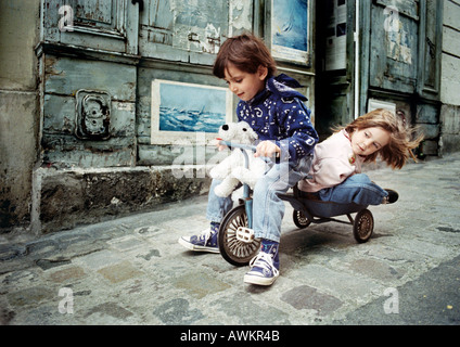 Little Boy riding triciclo con bambina sul retro Foto Stock