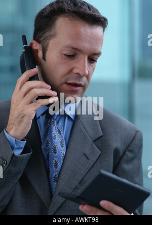 L'uomo tramite telefono cellulare mentre guarda il computer da tasca, ritratto Foto Stock