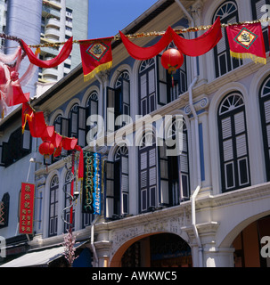 Fila di attraente ristrutturato edifici coloniali con luminosi bandiere rosse infilate attraverso la strada di Chinatown centro città Singapore Foto Stock