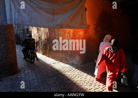 Motociclisti che guidano e donne che camminano attraverso un vicolo nello storico quartiere Medina di Marrakech, Marocco, Africa Foto Stock