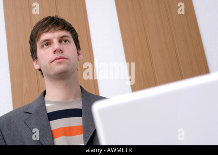 Giovane uomo in piedi di fronte a una scrivania, computer portatile in primo piano Foto Stock