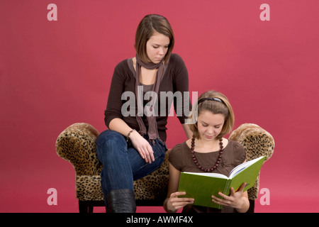 Due ragazze, pre-adolescenti, dai primi anni dell'adolescenza seduto su una tigre lettino stampa la lettura di un libro Foto Stock