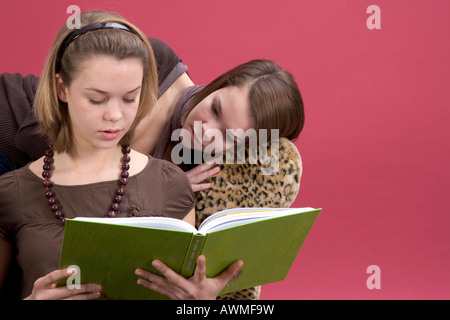 Due ragazze, pre-adolescenti, dai primi anni dell'adolescenza seduto su una tigre-divano stampa la lettura di un libro Foto Stock