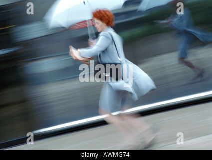 Donna in strada a piedi sotto ombrellone, offuscata Foto Stock