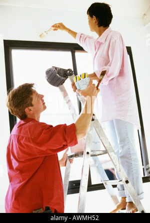 Donna parete di pittura, uomo con scaletta e la vernice può Foto Stock