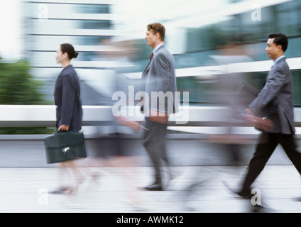 Tre persone che camminano con valigette, vista laterale, offuscata Foto Stock