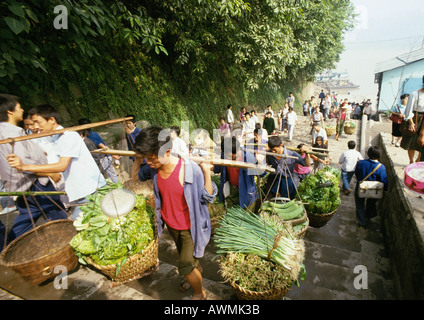 Cina, Sichuan, Chongqing, lavoratori che trasportano servirono cesti di produrre su gradini che portano dalla barca fluviale dock Foto Stock