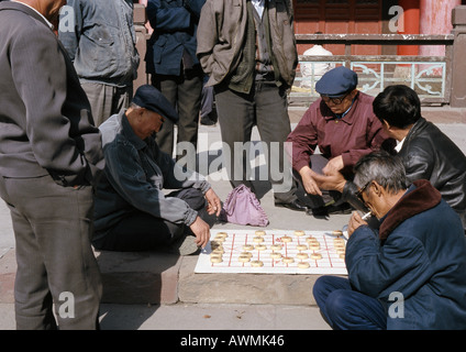 Cina, provincia dello Xinjiang, Urumqi, gruppo di uomini seduti sul marciapiede giocando xiangi sul marciapiede Foto Stock