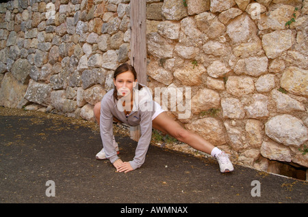 Giovane donna in abbigliamento sportivo stretching su una strada forestale Foto Stock