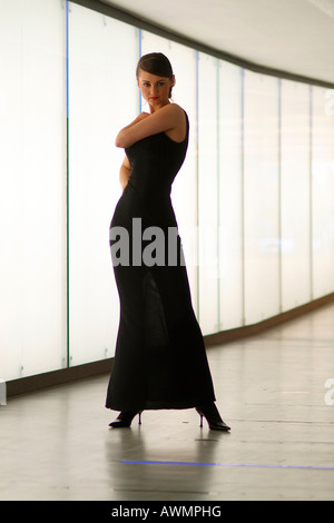 Giovane donna vestita di nero abito da sera in piedi di fronte a un acceso fino a parete in un passaggio pedonale Foto Stock