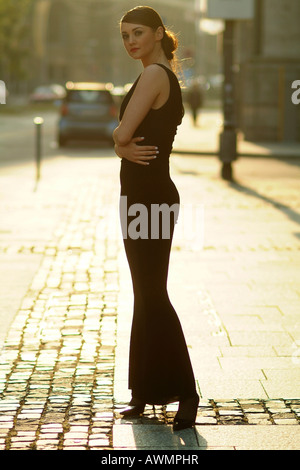 Giovane donna vestita di nero abito da sera in piedi su una strada acciottolata Foto Stock