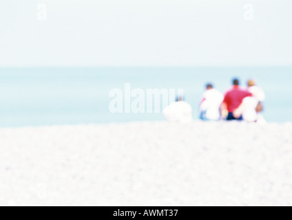 Gruppo di persone sedute sulla sabbia in spiaggia, vista posteriore, offuscata Foto Stock