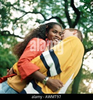 Coppia giovane abbracciando all'aperto, uomo whispering in giovane donna l orecchio a basso angolo di visione Foto Stock