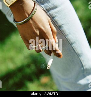 Giovane donna di mano azienda sigaretta accesa, close-up Foto Stock