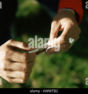 Giovane uomo le mani di sigaretta di rotolamento esterno, vicino. Foto Stock